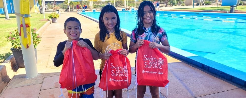 Three children by the pool with Swim and Survive bags