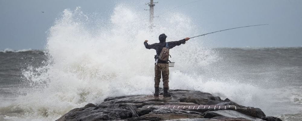 man fishing from rock with ocean wave breaking in front