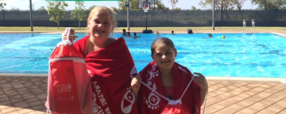 two girls holding their Swim and Survive packs and wrapped in Swim and Survive towels by the pool at Fitzroy Crossing