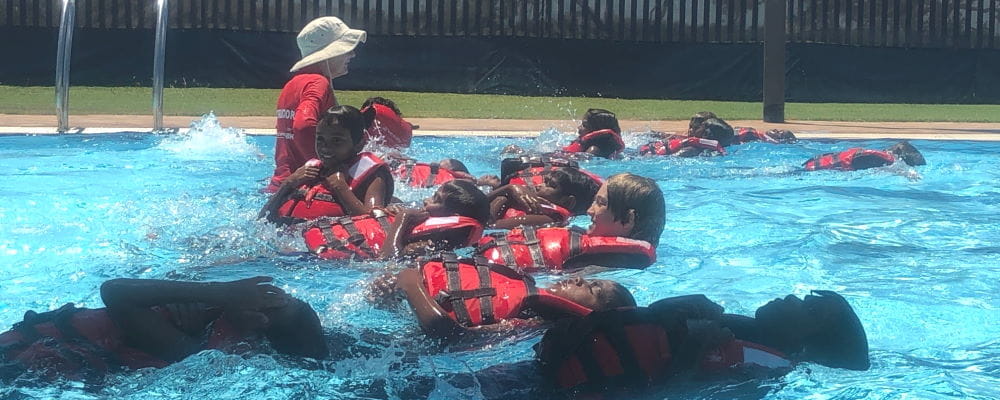 Swim instructor Susan Reeve in the water with a group of Aboriginal children wearing lifejackets