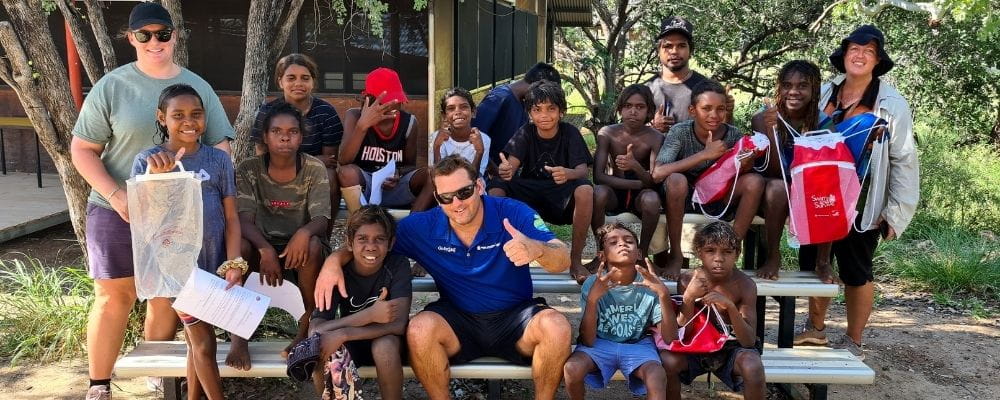 A group of Aboriginal children with Warmun remote pool manager Stephen Waterman by a tree
