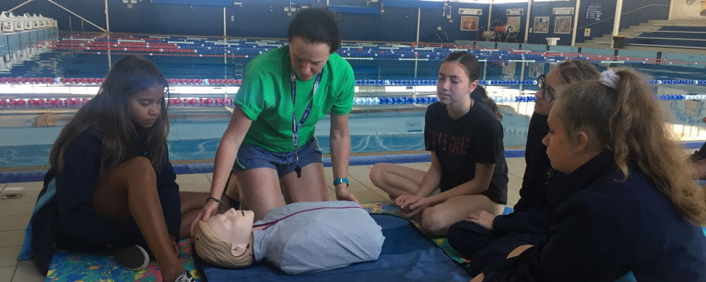 Four girls from Geraldton girls academy with an instructor demonstrating on a CPR manikin by the pool