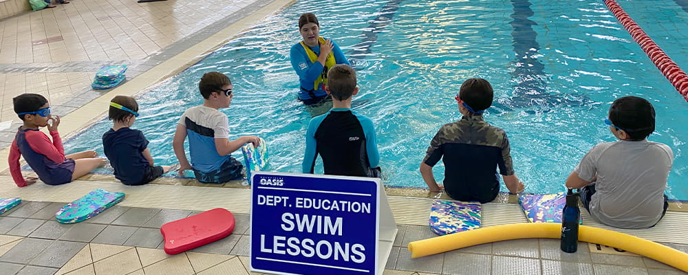 six swimming lesson students facing their instructor in a pool