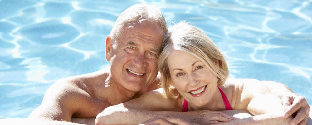 A man and woman leaning on the edge of a pool smiling at the camera