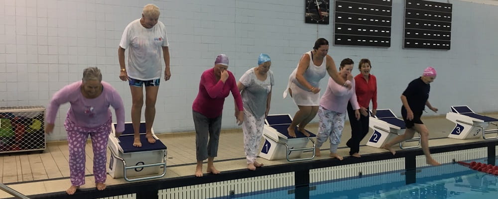 nine senior women jumping into a public swimming pool