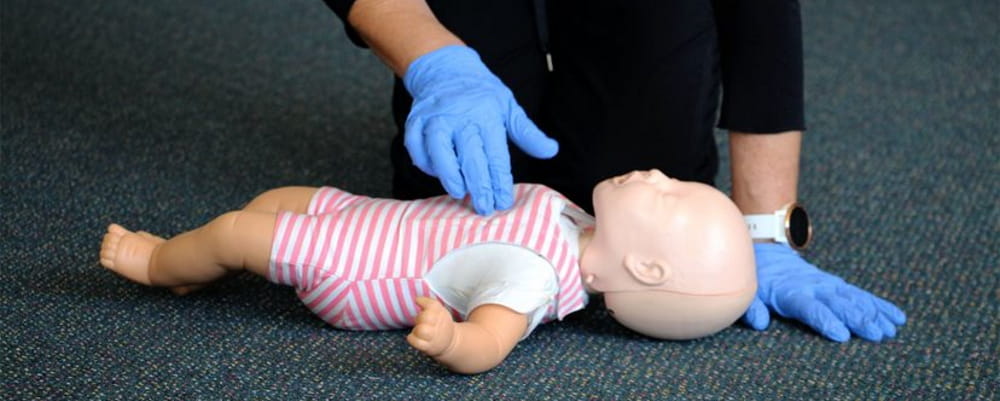A person performing CPR on an infant manikin