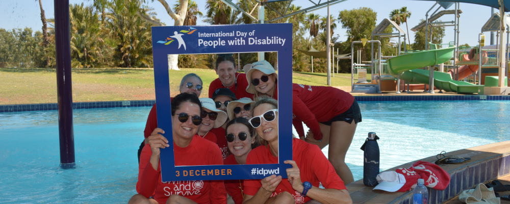 Swim instructors holding an international disability day sign, in the pool at Port Hedland