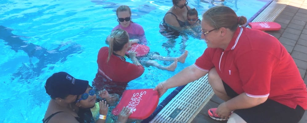 image of raelene leeds handing a swim and survive kick board to a participant in an infant aquatics class