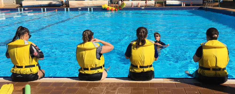 Four trainees sitting on the edge of the pool with lifejackets on