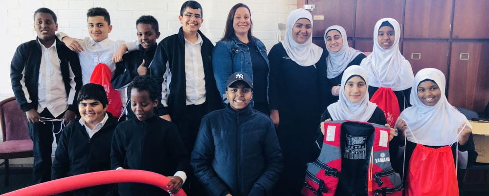 Children from the Australian Islamic College Kewdale with their water safety instructor, holding red pool noodles, lifejackets and Swim and Survive bags