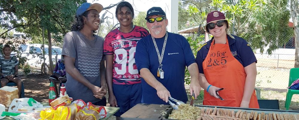 Jigalong Pool Manager David Lucas cooking sausages on the barbeque with two aboriginal youths and a woman looking on