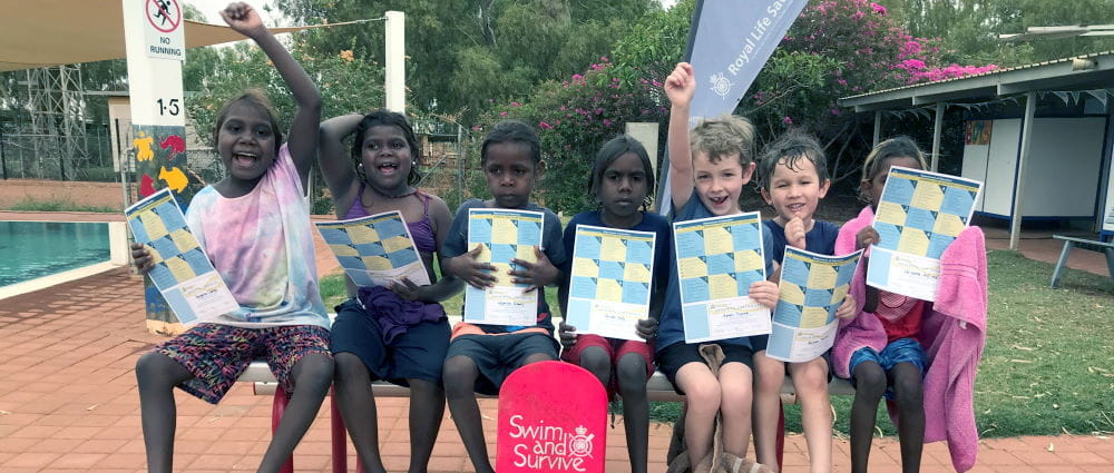 Eight childrne lined up holding their swimming certificates