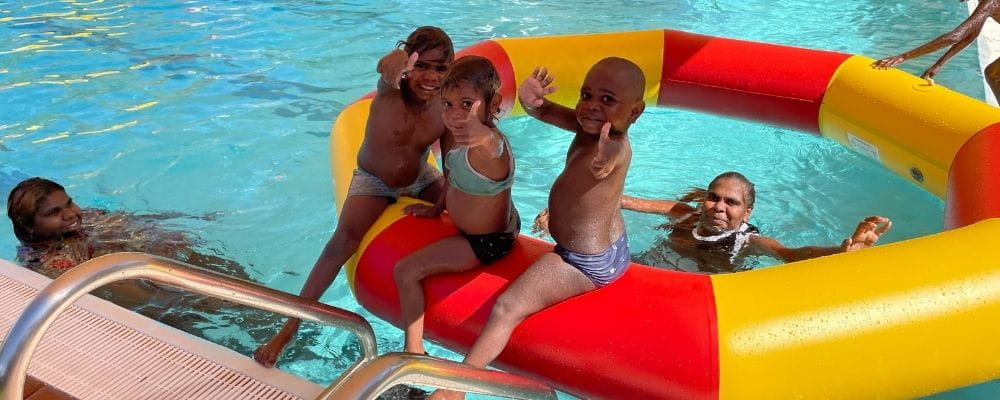 Aboriginal toddlers with their parents playing with a pool inflatable in the water