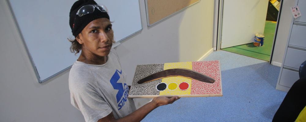 a Jigalong communioty member holding a boomerang in a display  made at the Jigalong Shed