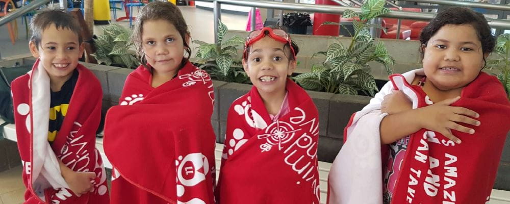 Four children wrapped in Swim and Survive towels standing by the pool