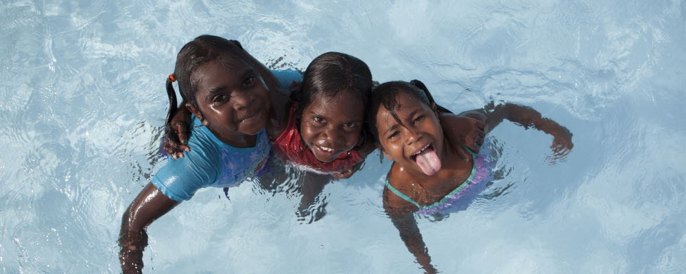 Three aboriginal girls in a swimming pool smiling at the camera
