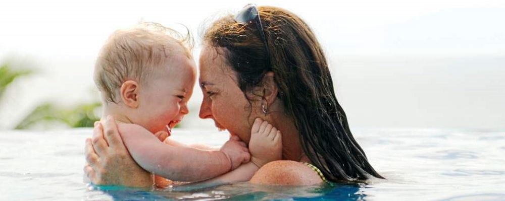Image of a mum holding a baby in the water, smiling at each other