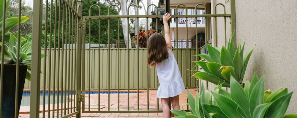 A toddler girl reaching up to try to open a pool fence