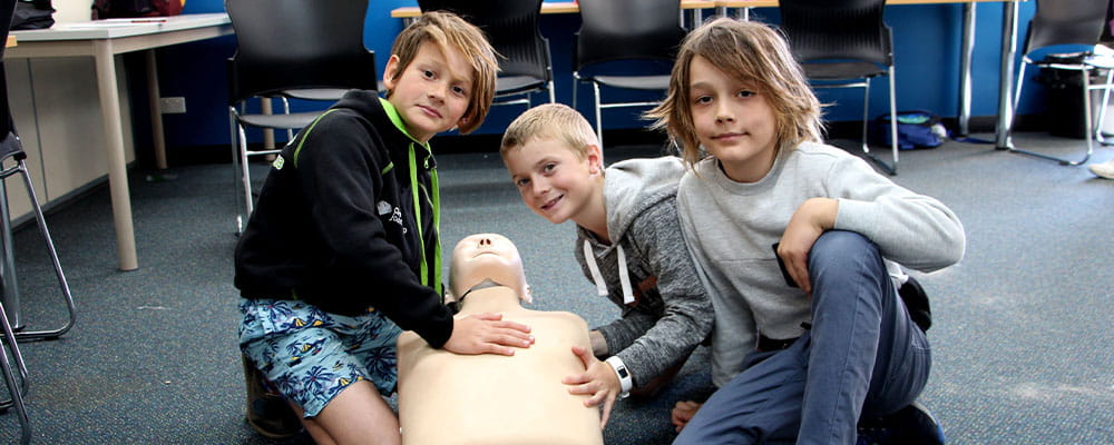 Three young boys practising CPR on a manikin