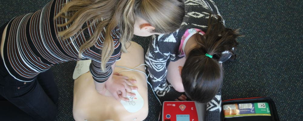 two girls performing CPR on a manikin using a defibrilator