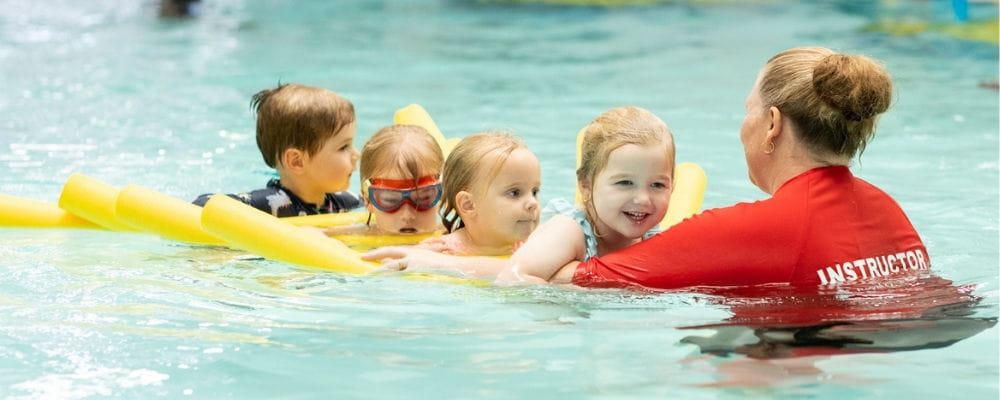 Swim instructor with four children floating on pool noodles