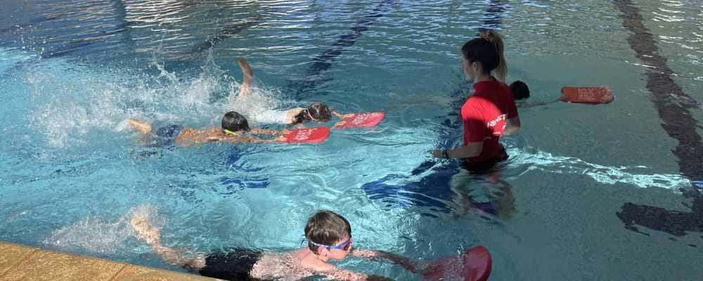 four children using kickboards at a swimming lesson