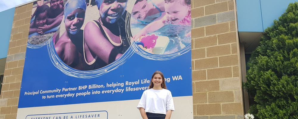 Lily Symons by the sign on the Royal Life Saving building that features her as a baby