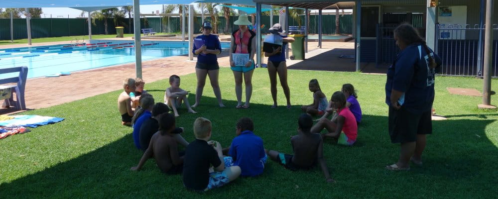 Swim instructors talking to children sitting on grass by the pool at Mount Magnet
