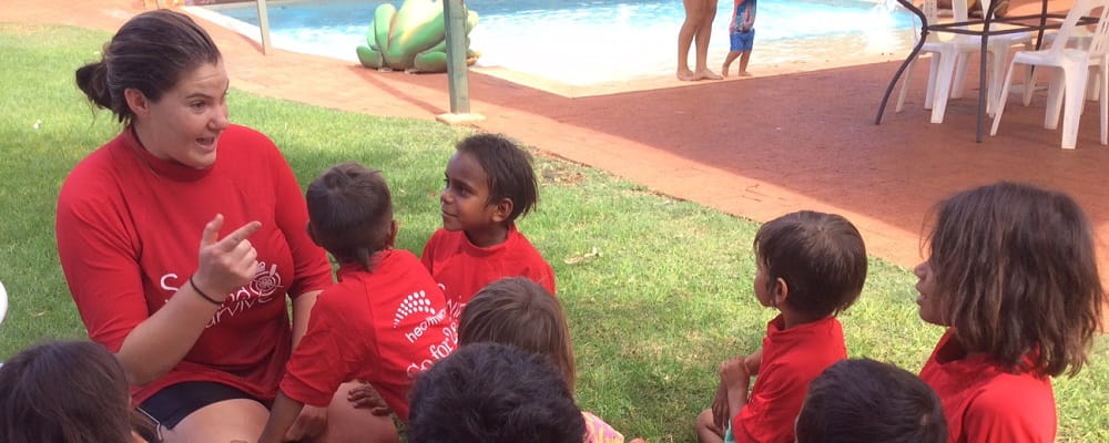 Aboriginal children wearing red Swim and Survive rashies with their instructor on the grass at the Newman Aquatic  Centre