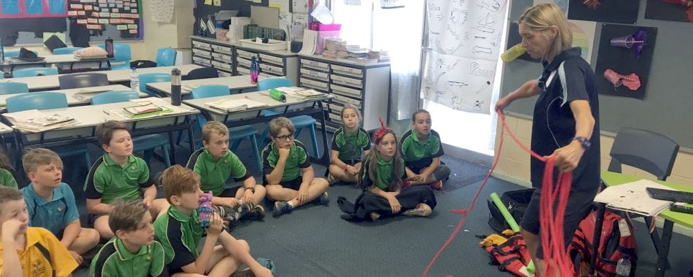 Children sitting watching Jacqui Forbes show them how to do a rope throw