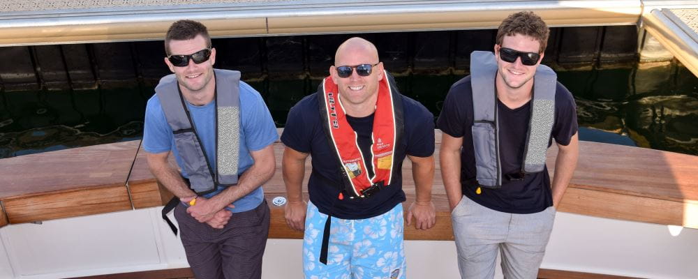 Three men wearing lifejackets, standing on a boat
