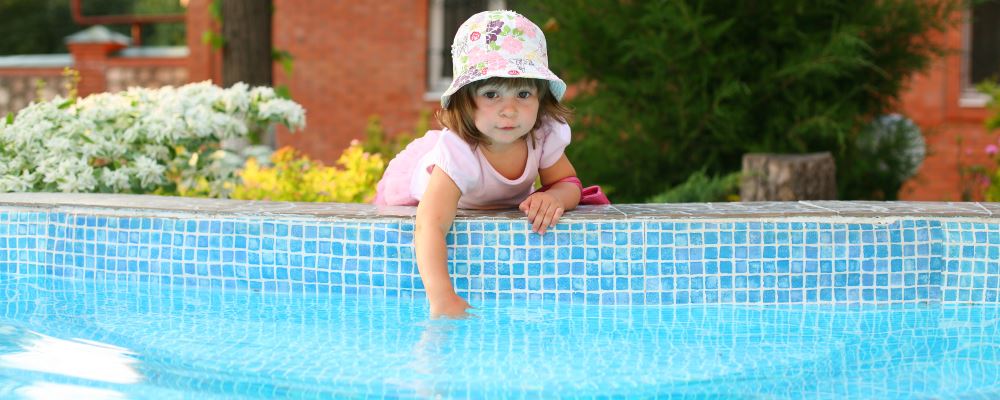 A toddler girl leaning over the edge of a pool to touch the water