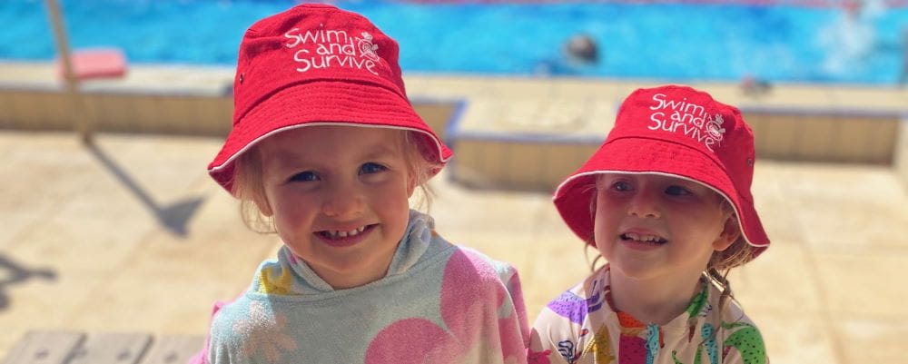 Two little girls by the pool wearing poncho towels and Swim and Survive hats