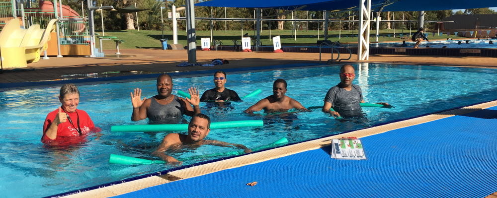A swim instructor in the pool with a group of multicultural men