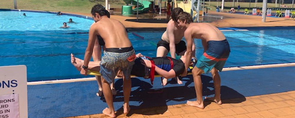 A group of trainees lifting someone out of a pool on a spineboard