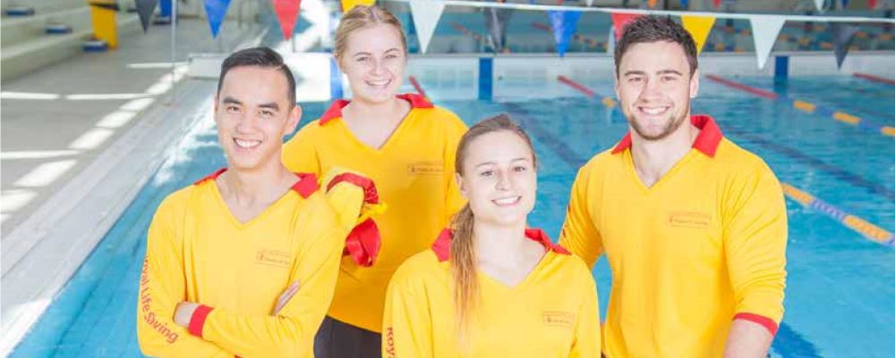 Image of four lifeguards standing by a pool smiling at the camera