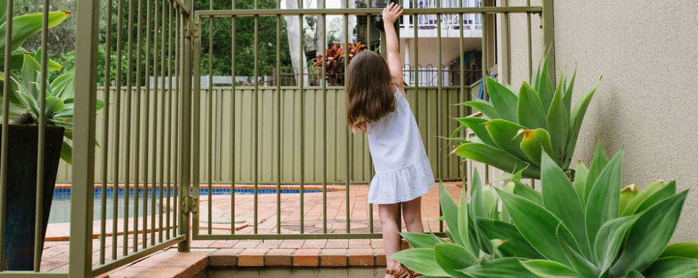 A little girl at a pool gate, reaching up for the latch