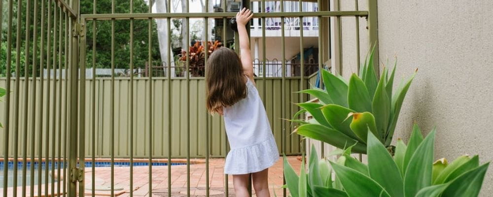 A young girl reaching up to the latch of a pool gate