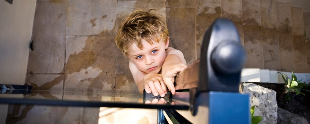 image of young boy reaching up to pool gate latch and looking at camera