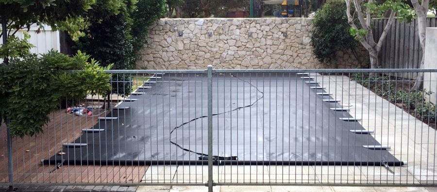 A home pool covered with amn Elite Pool Cover and guarded by a fence.