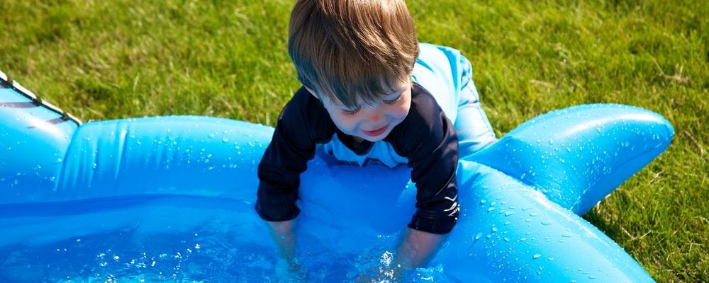 image of toddler leaning into a portable pool, splashing the water