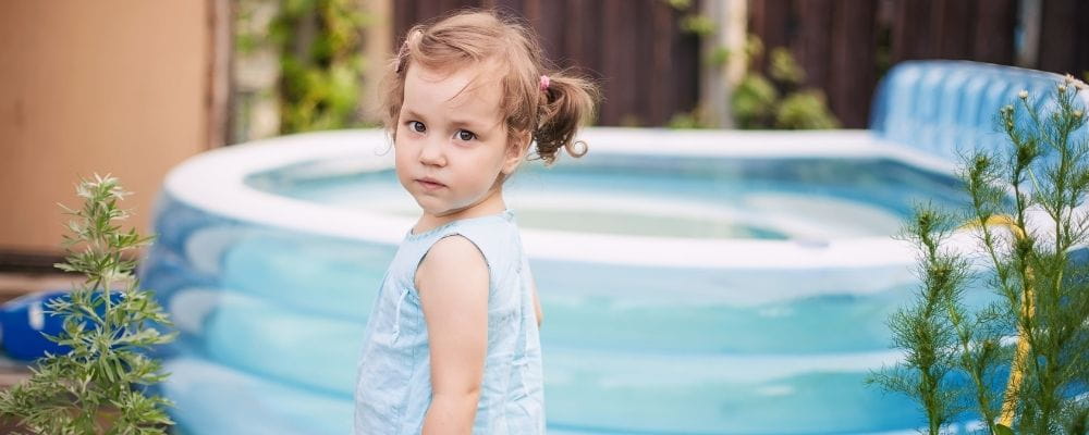 A toddler girl standing in front of a portable pool