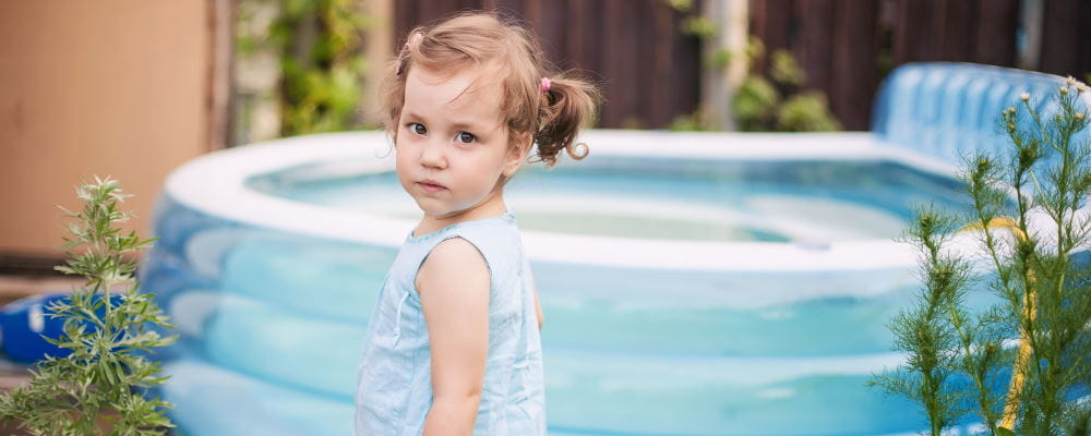 A toddler girl standing by a portable pool in a backyard