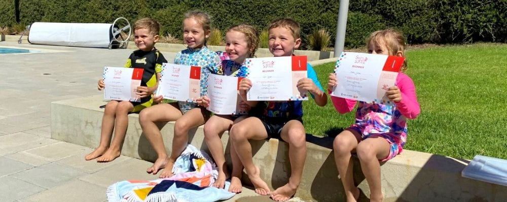 Five children wearing bathers nad holding their swimming certificates