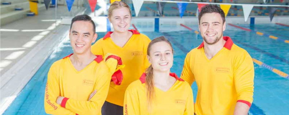 A group of 4 lifeguards standing by a pool