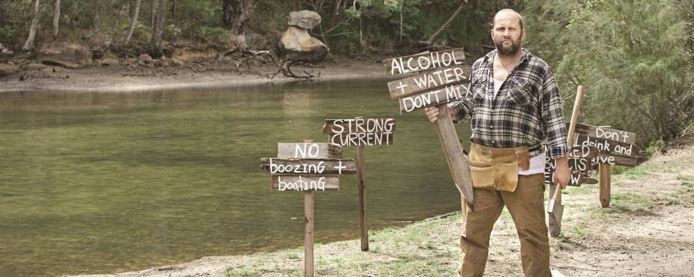 A man wearing a flannel shirt and holding an axe with signs warning about the dangers of alcohol and water
