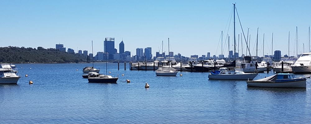 An image of the Swan River with boats in the foreground and the Perth city skyline in the distance