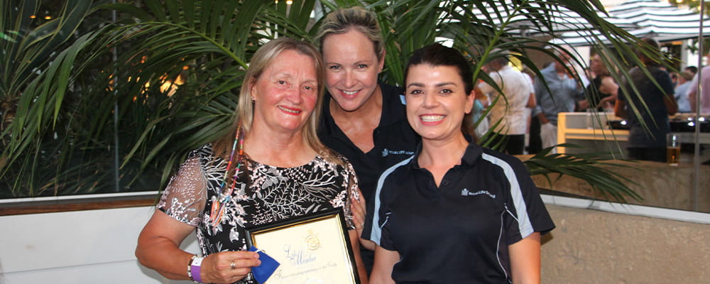Trainer Sallie Watson holding her life member award with two royal life saving employees