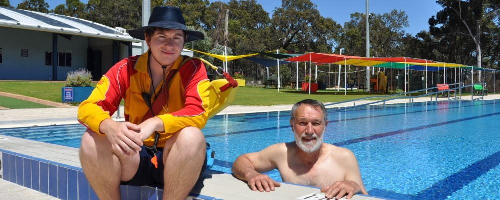Trainee Duty Manager/Lifeguard Tyler Parish sitting on the pool edge alongside Deputy Shire President Patrick Bertola in the water
