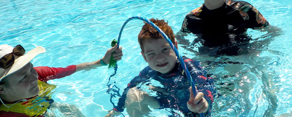 A swim instructor in the pool with a student going through a hoop